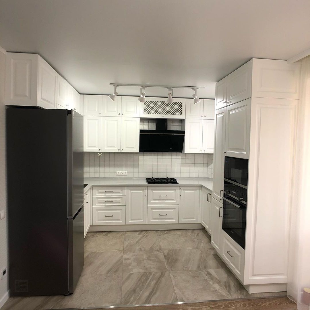 Фото п-образная белая светлая кухня с крашеными фасадами в неоклассическом стиле c акриловой столешницей