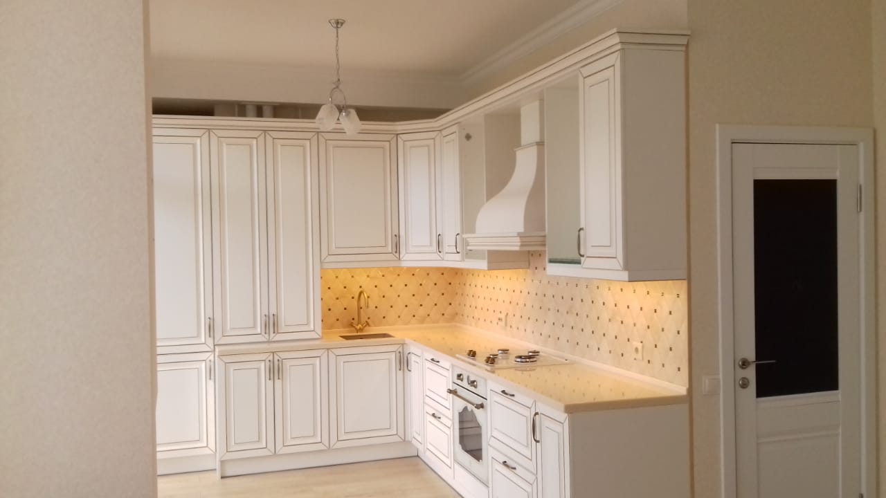 Белая угловая кухня с крашеными фасадами в классическом стиле c акриловой столешницей