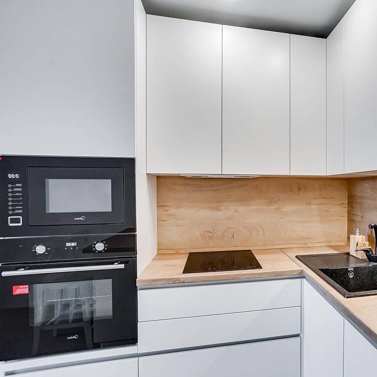 Фото угловая белая древесная матовая кухня с крашеными фасадами в стиле Хай-Тек и в стиле Минимализм с пластиковой столешницей