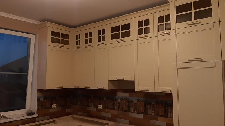 Фото угловая трехъярусная бежевая матовая светлая кухня с крашеными фасадами в неоклассическом стиле c акриловой столешницей