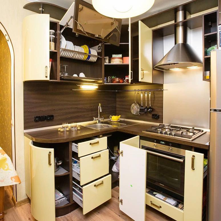Фото угловая бежевая древесная кухня с фасадами МДФ-ПВХ в стиле Хай-Тек с пластиковой столешницей