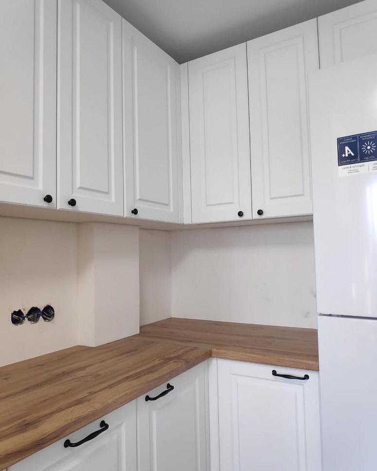 Фото угловая белая матовая кухня с фасадами МДФ-ПВХ в неоклассическом стиле с пластиковой столешницей